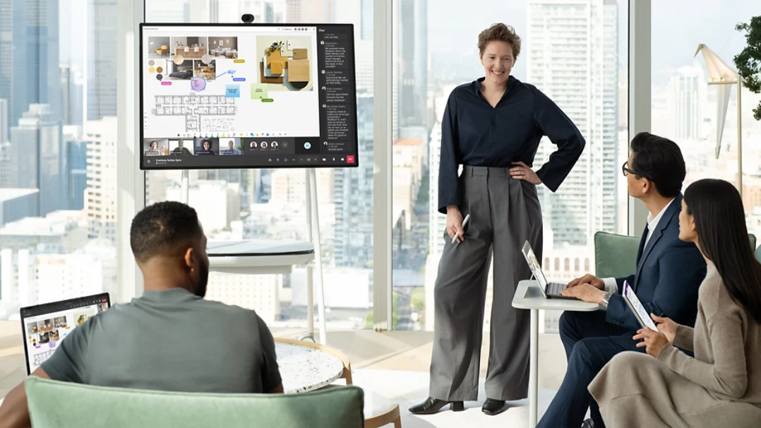 An office room with four workers around a table and a mounted Hub 3 device on a Teams call