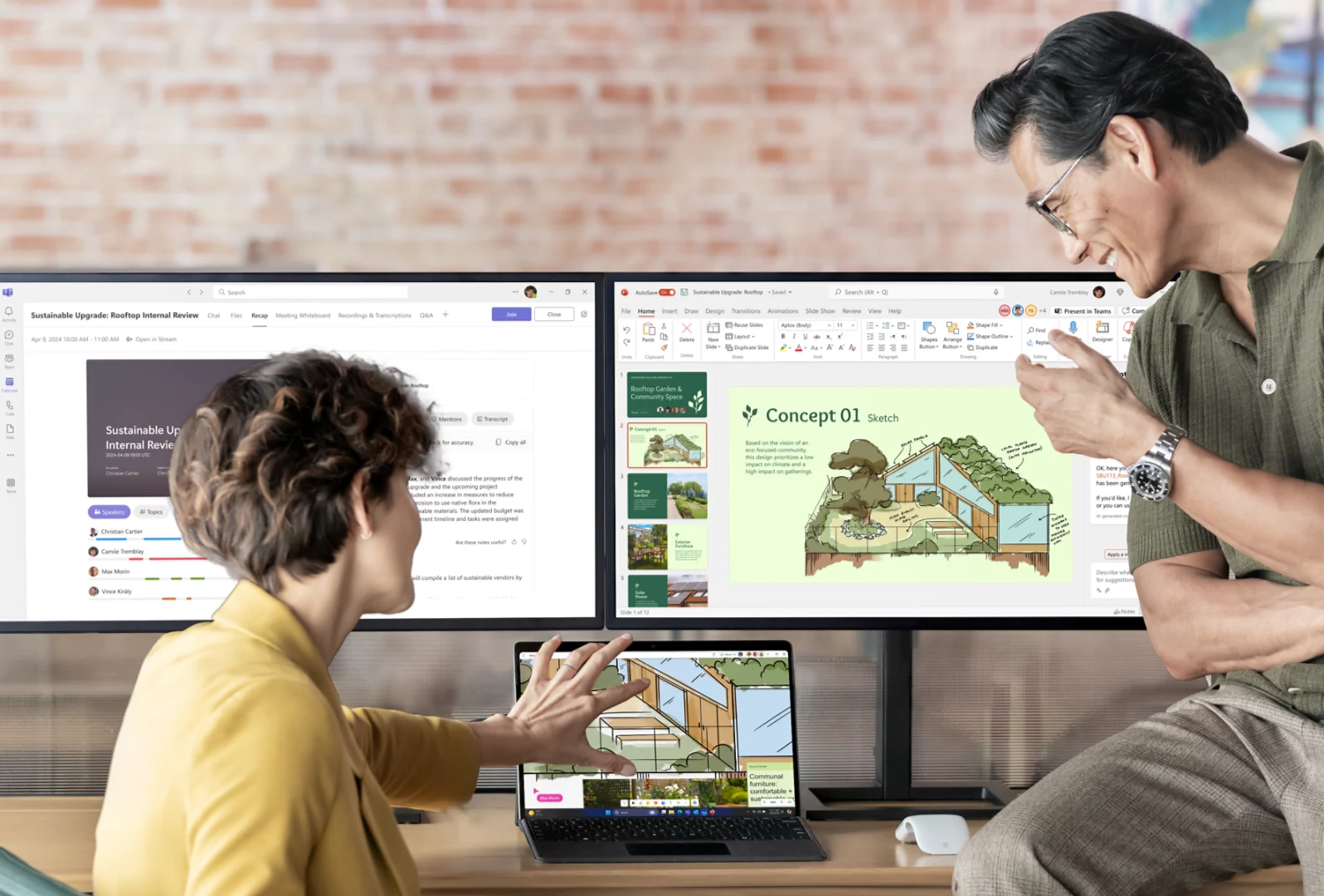 Man and woman at a desk looking at Surface Pro 10 that is connected to 2 monitors displaying Microsoft 365 applications