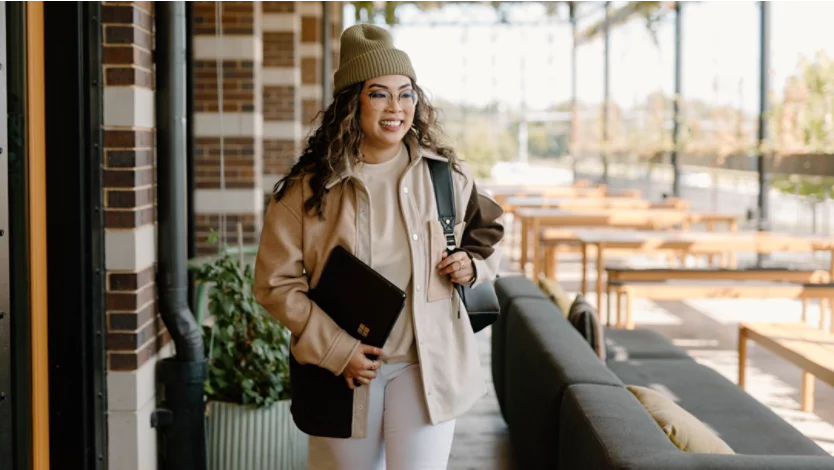 Woman in outdoor restaurant holding Surface laptop and backpack