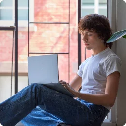 Jovem sentado em uma janela aberta segurando um PC