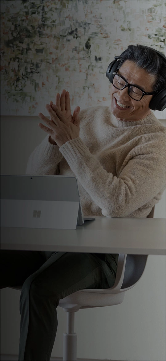 En mann sitter på hjemmekontoret og bruker sin Surface Pro 9 mens han har på Surface Headphones 2+