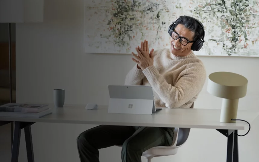 自宅のオフィスに座り、Surface Headphones 2+ を装着して Surface Pro 9 を楽しむ男性