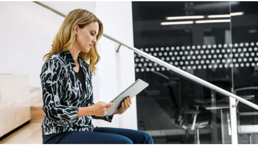 A woman reads from her tablet while seated in an office on stairs.