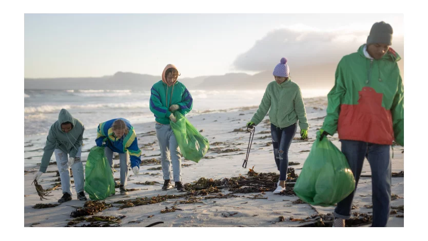 Un grupo de cinco jóvenes voluntarios limpiando una playa.