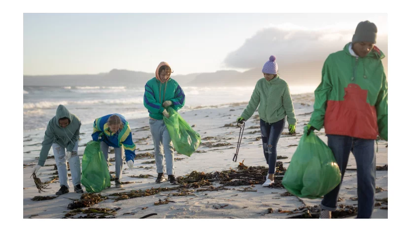 En gruppe på fem unge frivillige rydder en strand.