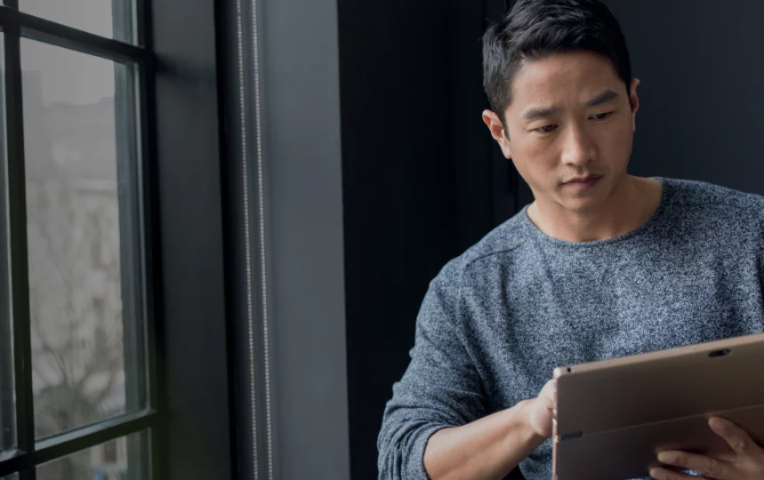 Primer plano de un empresario usando una tableta junto a una ventana.