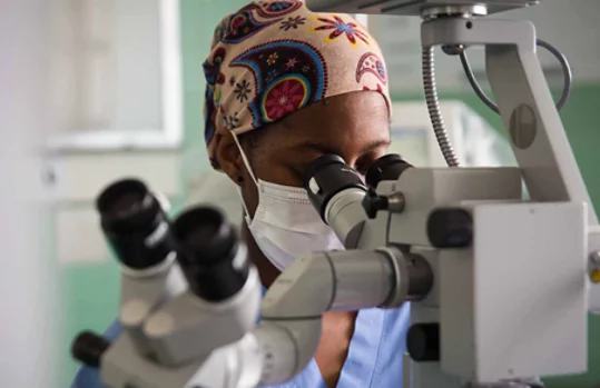 Una persona que lleva un pañuelo en la cabeza y una mascarilla médica mira a través de un microscopio