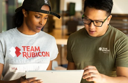 Miembros del equipo de Team Rubicon mirando juntos una tableta.