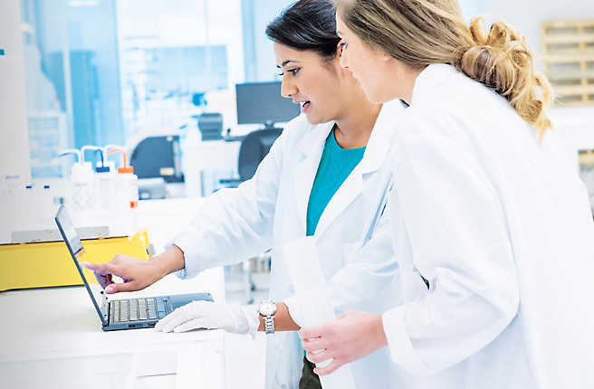 Dos mujeres con batas de laboratorio trabajando en un portátil