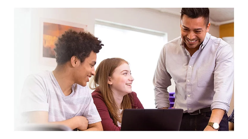 Teacher working with two young adults on a laptop