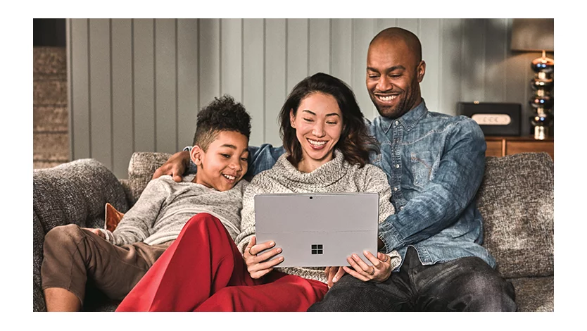 A family of three watching on their tablet device together at home on their couch.