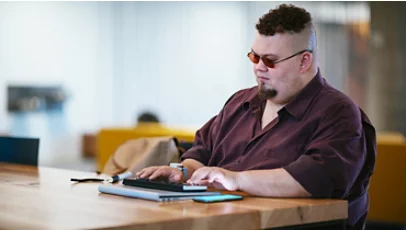 A man who is blind, types on a braille keyboard while also working through a mobile phone.
