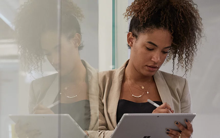 Woman in an industrial office setting leaning against a glass wall while holding a tablet and stylus.