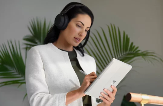 Una persona con Surface Headphones 2+ usa su Lápiz para Surface para navegar por Surface Go 4 en modo tableta en el trabajo