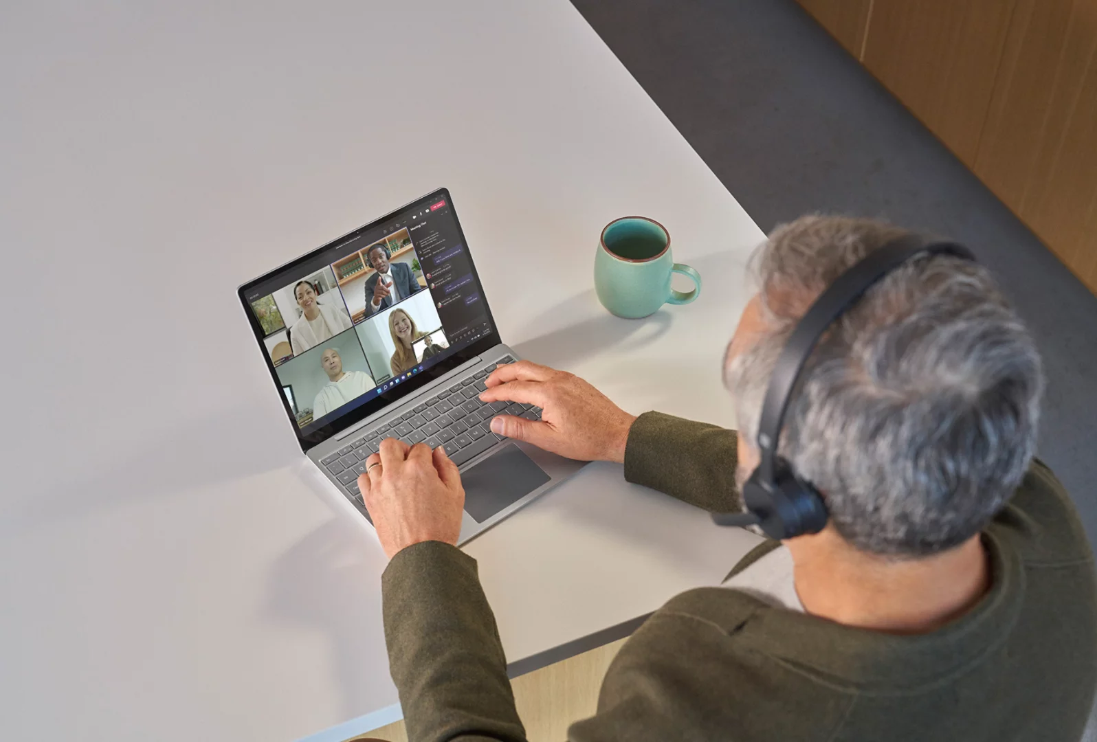 A top-down view of a person wearing Surface Headphones 2 while on a Teams meeting on their Surface Laptop Go 3