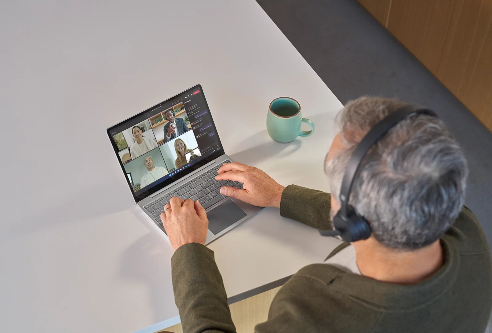 Vista dall'alto di una persona con le cuffie Surface Headphones 2 che partecipa a una riunione di Teams sul suo dispositivo Surface Laptop Go 3