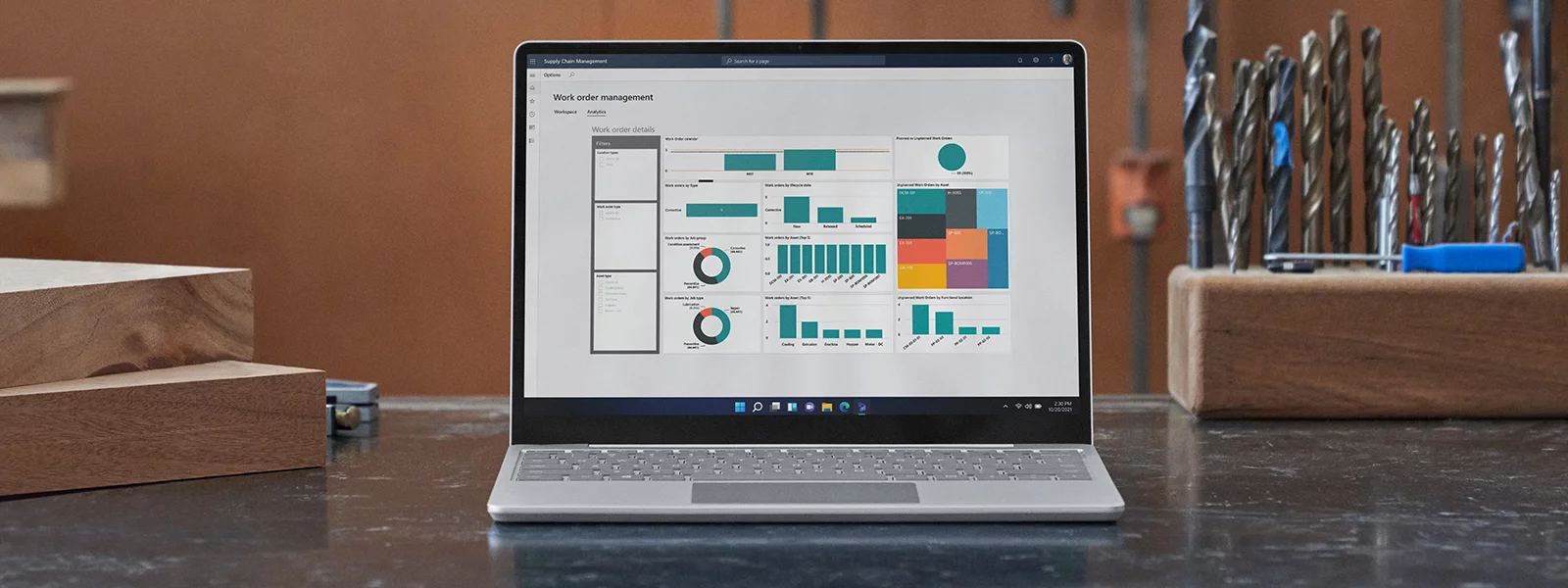 A front-facing Surface Laptop Go 3 is observed on a desk in a wood shop setting. Drill bits are placed nearby.