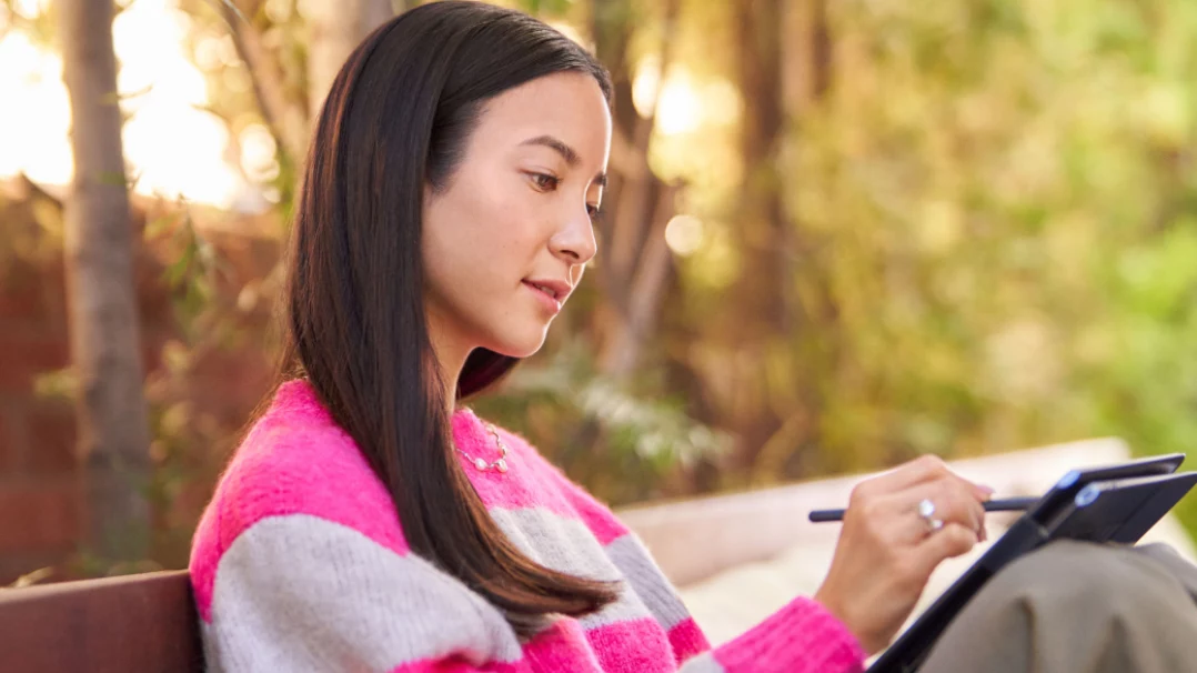 Une femme assise sur un banc, dans un parc, utilisant un stylet numérique avec son PC