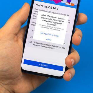 A man&#x27;s hand holds a new iPhone with a prompt to allow or not allow Facebook to track activity on the screen.