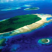 Aerial view of island, part of reef formtion, South Pacific, shows water on all sides, smaller islands in background and one in foreground.