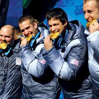 Former U.S. Army World Class Athlete Program bobsledder Steven Holcomb, left, and teammates Justin Olsen, Steve Mesler and Curt Tomasevicz bite their gold medals Saturday night at Whistler Medals Plaza after winning the Olympic four-man bobsled, 2010.