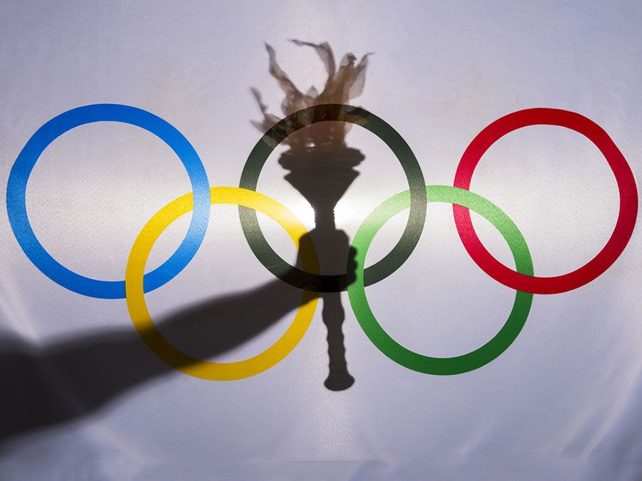 Silhouette of hand holding sport torch behind the rings of an Olympic flag, Rio de Janeiro, Brazil; February 3, 2015.