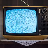 1970s style television set with static on the screen, on a small table with a doily underneath. (retro style)