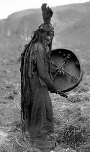 Mongolian shaman wearing a ritual gown and holding a drum with the image of a spirit helper, c. 1909.