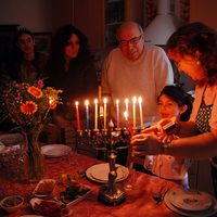 Judaism - Hanukkah. Jewish family lighting a candle on a menorah. Also called Festival of Lights or Feast of Lights.