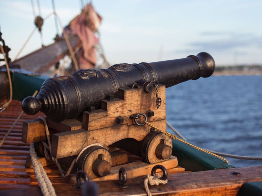 Old medieval wooden pirate military war ship with a cannon on the deck pointed out and aiming