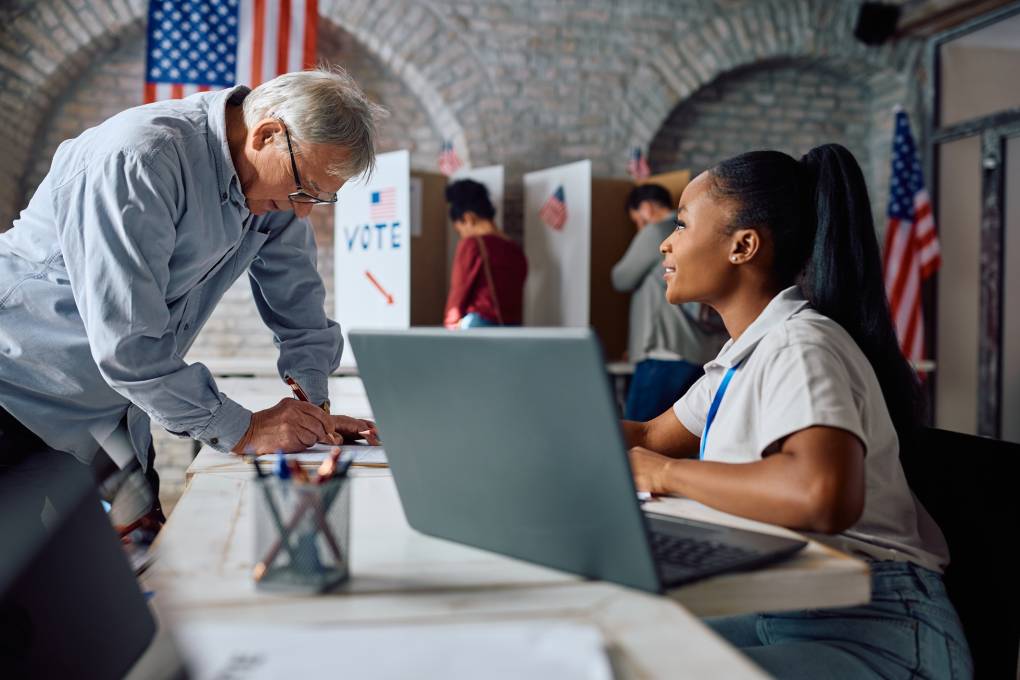 A Black woman assists a senior white man in signing up to vote for the elections.