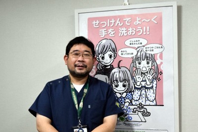 漫画家の羽海野チカさん描き下ろしポスターをバックに立つ大阪大大学院の忽那賢志教授＝大阪府吹田市の大阪大で2023年12月26日、西田佐保子撮影