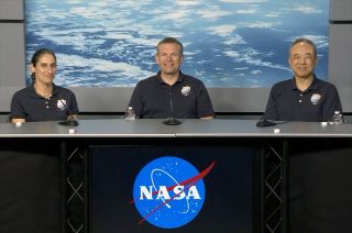 two men and a woman in blue polo shirts sit at a table with a photo of earth as seen from space in the background