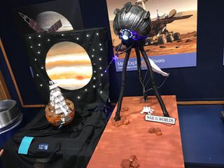 A black pumpkin on three ominous legs aims a light at a pumpkin decorated like a warship. A picture of Mars looms in the background.