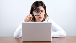 Woman looking at a laptop screen through a magnifying glass held up to her face