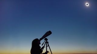 a young woman watches a solar eclipse through binoculars.