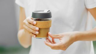 Someone wearing a white t-shirt holding and small travel mug