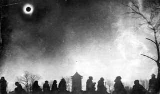 A moody image showing black silhouettes of people gathered beneath a fully eclipsed sun.