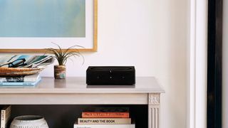 the sonos amp in black on a console table in a living room next to a small plant