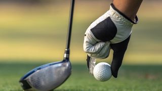 A golfer placing a ball on a tee while wearing a golf glove