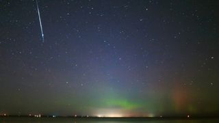 night sky with large white streak in upper left corner (meteor) and a faint green glow of aurora at the base of the image.