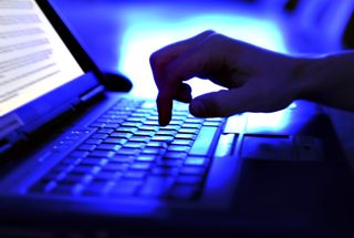 person typing on a laptop keyboard in a blue-lit room