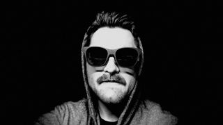 Black and white photo of a man with mustache wearing AR smart glasses and a hoodie.