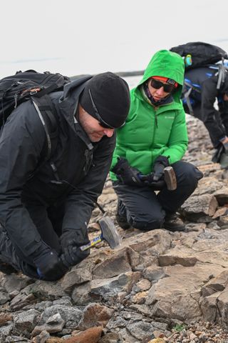 two people in warm winter outdoor gear smash rocks with hammers