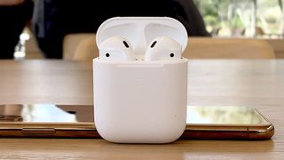 AirPods 2 in a charging case against an iPhone X on a wooden table