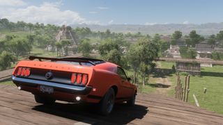 A screenshot from Forza Horizon 5 showing a Ford Mustang on a hill above Mayan ruins in Mexico