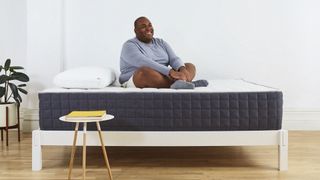 Best mattress for heavy people: a man in a blue shirt sits on the Helix PLUS mattress