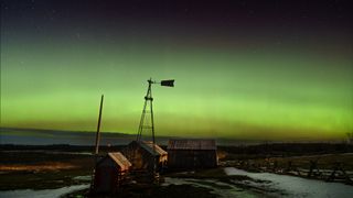 Green band of aurora light in the sky above a rural building.