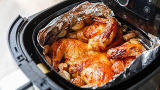 A chicken with potatoes in an air fryer basket