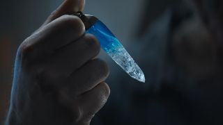 Still from the Star Wars T.V. series Andor. here we have a close up of a hand holding a blue-ish crystal about the lengeth and thickness of an adult finger.